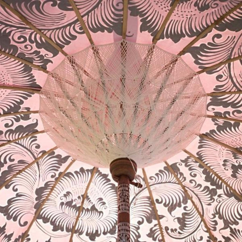 Stevie Round Bamboo Parasol- Pale pink twill garden parasol with floral design hand painted in silver ink. The pole is made from hand-carved durian wood pole with silver paint and finial, the pole join and pegs are made from solid brass with white threading, bamboo spokes.