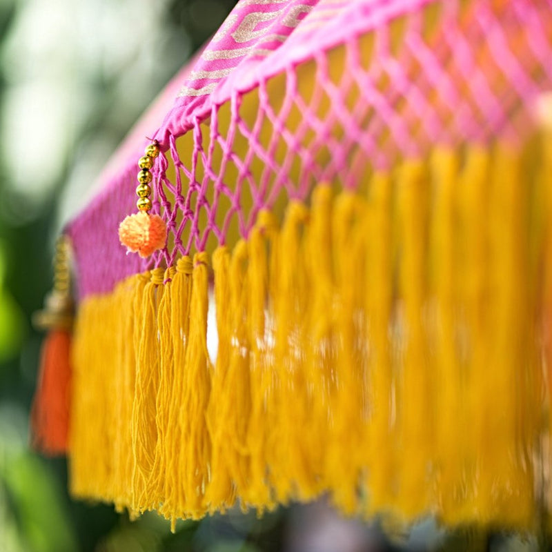 Whitney- East London Parasol Company pink Bali garden umbrella with yellow and orange tassels, pom poms and fringing. Stunning, colourful parasol for an elegant summer garden. 