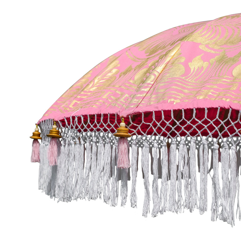 Heidi Round Bamboo Parasol is a blossom pink twill umbrella with lotus design hand-painted in gold ink. White threading inside and bamboo spokes. The pole is made from hand-carved durian wood pole with gold paint and finial, the pole join and pegs are made from solid brass. The fringing is in white with gorgeous white tassels and gold beading.