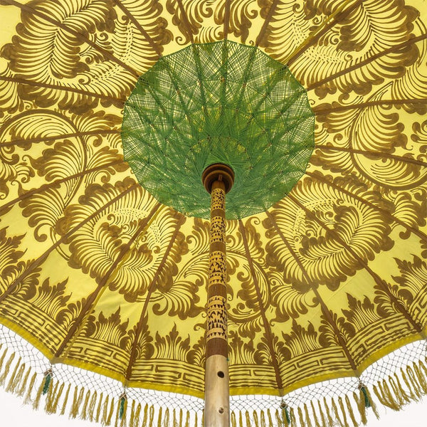 Goldie Round Bamboo Parasol is a lovely yellow twill with lotus design hand-painted in gold ink. Sea green threading and bamboo spokes. The pole is made from hand-carved durian wood pole with gold paint and finial, the pole join and pegs are made from solid brass. The fringing is in shades of vibrant primrose yellow with muted green tassels to match the interior threading.