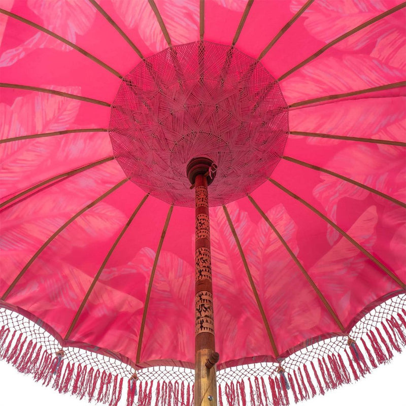 Pink Nina Round Bamboo Parasol- Show-stopping bright pink waterproof canvas umbrella digitally printed with a palm print and banana leaf design in shades pink and blue accents. This is a unique piece and utterly tropical flamboyant garden parasol, blending together the best of modern textile technology and traditional craftsmanship.