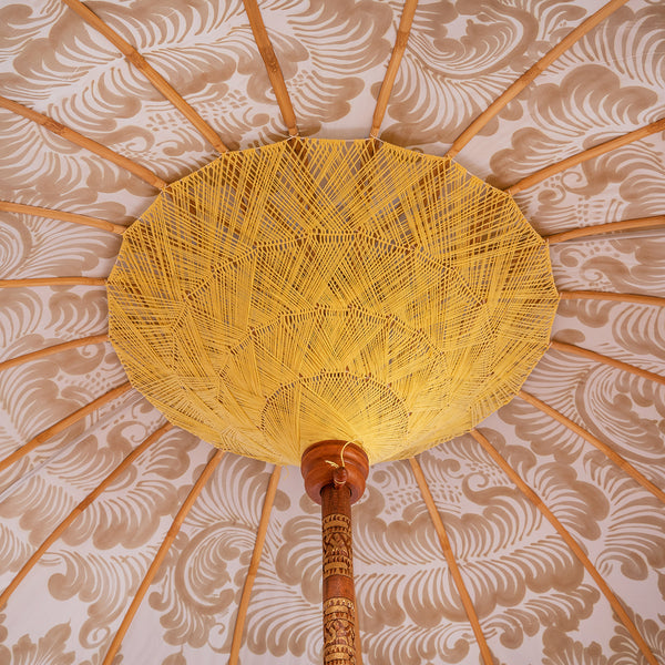 Hugo Round Bamboo Parasol is a pastel heaven with the light blue twill with lotus design hand-painted in gold ink. Yellow threading inside and bamboo spokes. The pole is made from hand-carved durian wood pole with gold paint and finial, the pole join and pegs are made from solid brass. The fringing is in coral with chic yellow tassels and gold beading.