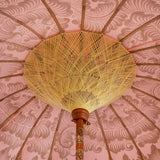 Rosanna Round Bamboo Parasol's canopy is a gorgeous pastel pink with lotus design hand-painted in gold ink.  Inside the threading is light yellow, and the fringe is a combination of mint green and light yellow tassels. The pole is made from hand-carved durian wood pole with gold paint and finial, the pole join and pegs are made from solid brass.