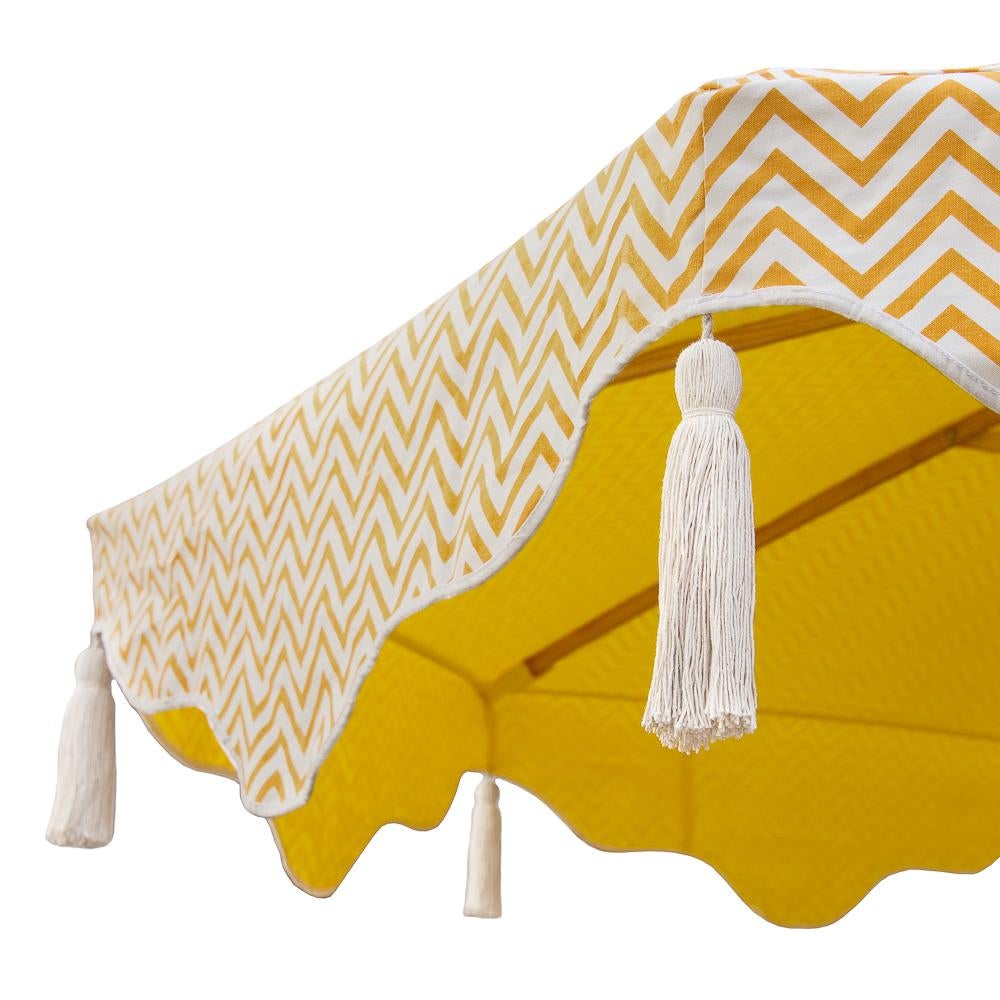 East London Parasol Company. Big Orange Aretha, stunning 3m wooden frame garden parasol. Natural waterproof cotton canvas with printed orange zig zags and yellow interior, with natural cotton tassels. The edges are an arabian-influenced shape. The canopy is removable. The ultimate garden decoration. Perfect show stopping garden umbrella for an elegant dining area or pool, or beside a sun lounger, for an event or wedding. Luxurious, flamboyant and colourful garden accessories.