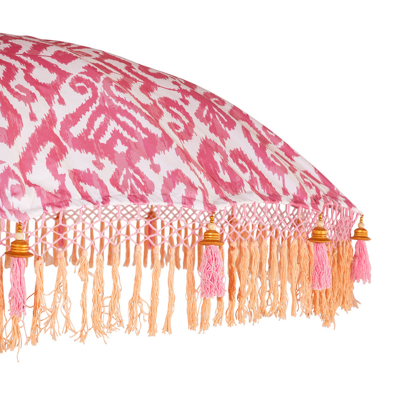 Sophia Round Bamboo Parasol's canopy is a glamorous digitally printed pink and white ikat print. Inside the threading is vibrant lemon yellow, and the fringe is a combination of coral fringing and pink tassels. The pole is made from hand-carved durian wood pole with gold paint and finial, the pole join and pegs are made from solid brass.