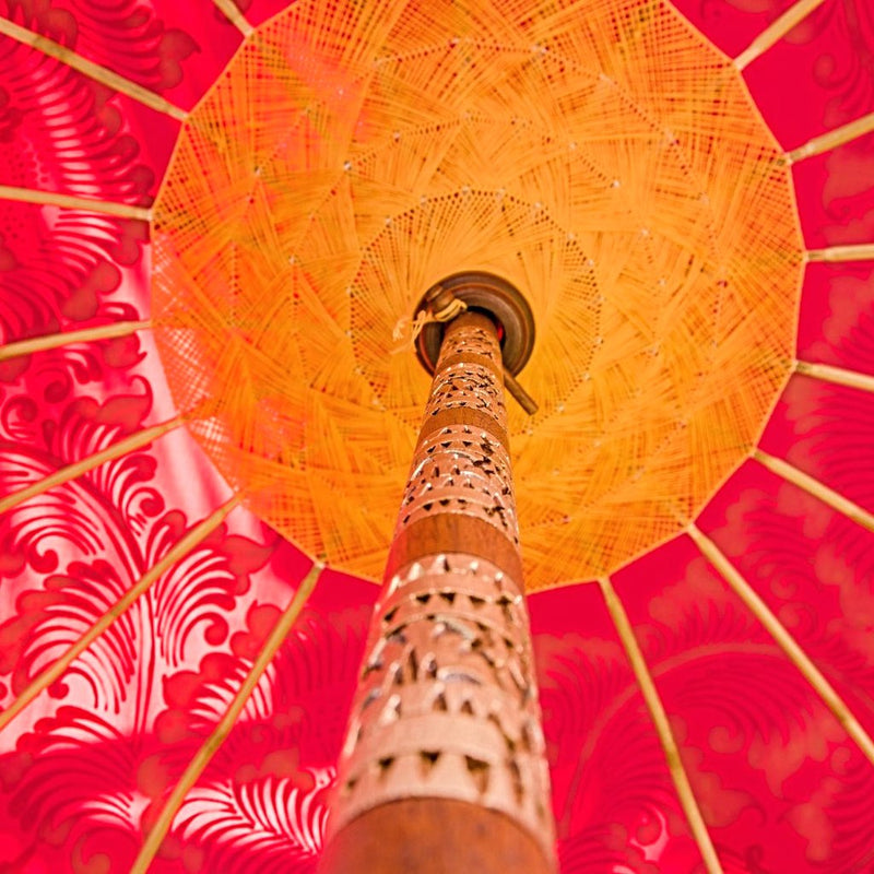 Whitney Round Bamboo Parasol- The stunning gold pattern is hand-painted by artisans. The parasol has bamboo spokes and yellow threading. The fringing is yellow cotton with orange pom poms and tassels. The pole is made from hand-carved durian wood pole with gold paint and finial, the pole join and pegs are made from solid brass.