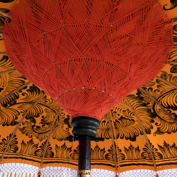 Augusta Round Bamboo Parasol has dark orange threading inside and bamboo spokes. The pole is made from hand-carved durian wood pole with gold paint and finial, the pole join and pegs are made from solid brass. The fringing is in orange with yellow tassels and beading. These are handmade items and there may be some variation in colour.