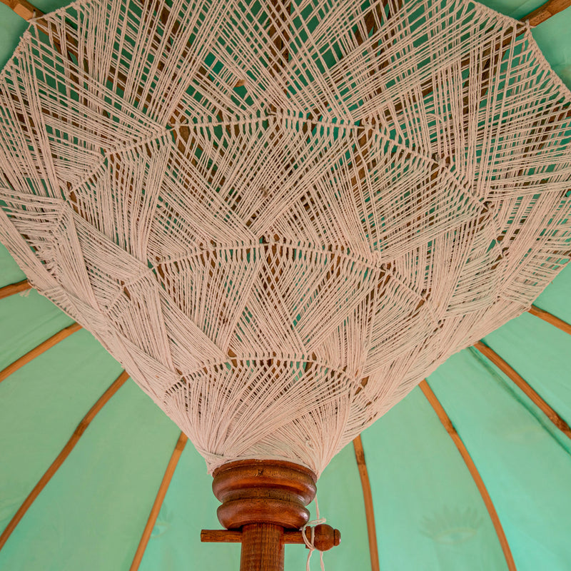Catherine Round Bamboo Parasol has an evil eye printed canopy on turquoise with orange threading and white fringing. pole is made from hand-carved durian wood pole with gold paint and finial, the pole join and pegs are made from solid brass.
