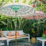 Lifestyle image of outdoor Cher and Stevie Round Bamboo Parasol. Beautiful cream, silver and blue garden parasol. Hand-painted with silver ink by artisans in Bali. The pole is made from hand-carved durian wood pole with silver paint and finial, the pole join and pegs are made from solid brass.