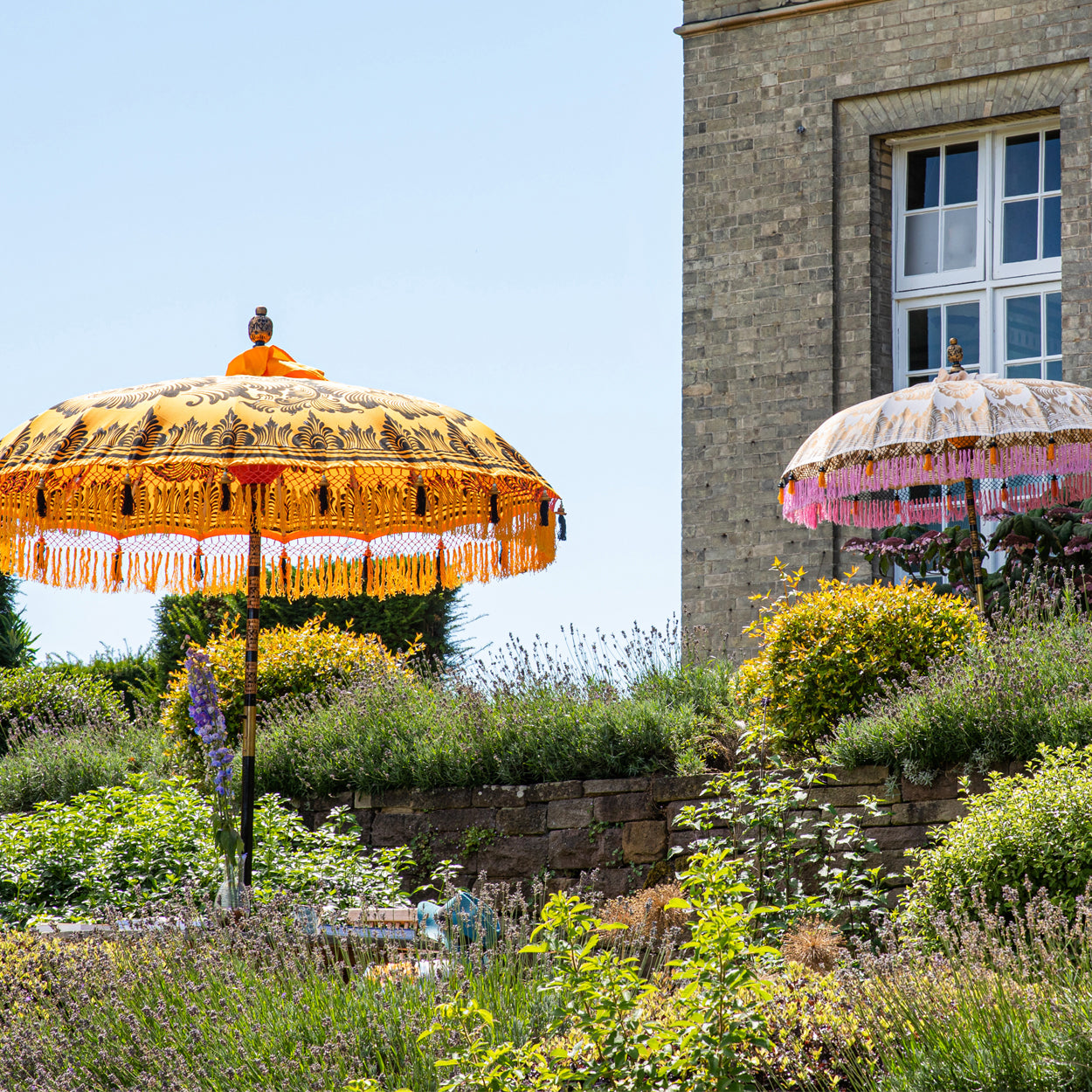 Lifestyle image of Augusta & Helena Round Bamboo Parasol - soft beige twill with lotus design hand-painted in gold ink. Inside the threading is vibrant tangerine orange, and the fringe is a combination of peony pink, black and orange tassels.