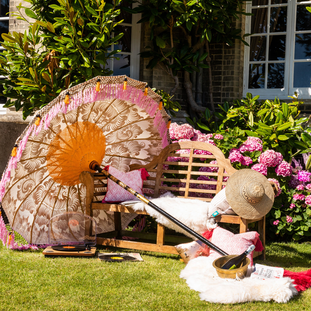 Lifestyle image of Helena Round Bamboo Parasol - soft beige twill with lotus design hand-painted in gold ink. Inside the threading is vibrant tangerine orange, and the fringe is a combination of peony pink, black and orange tassels.