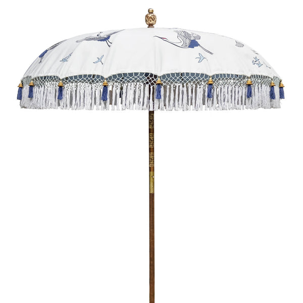 Lexi Round Bamboo Parasol -Digitally printed off-white with a design of soaring cranes in shades of indigo and grey, inspired by Japanese woodcuts. The parasol is printed on waterproof canvas, lined with heavenly blue with French-blue threading and bamboo spokes. The pole is made from hand-carved durian wood pole with gold paint and finial, the pole join and pegs are made from solid brass.