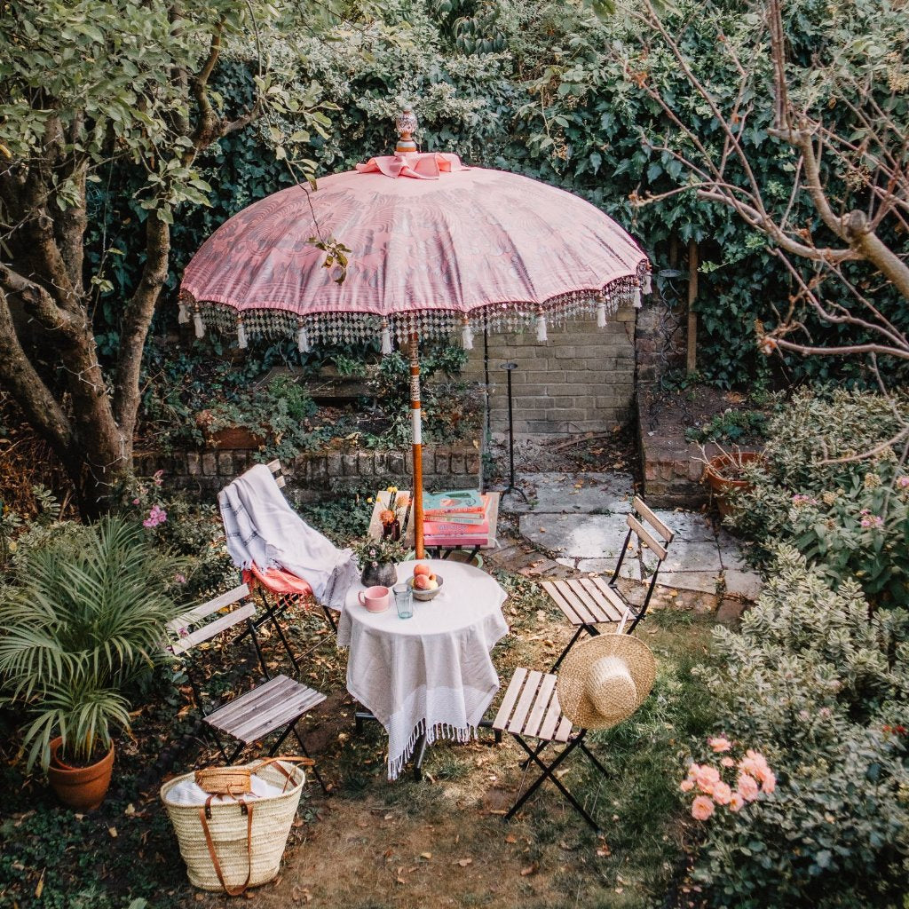 Stevie Round Bamboo Parasol- Pale pink twill garden parasol with floral design hand painted in silver ink. The pole is made from hand-carved durian wood pole with silver paint and finial, the pole join and pegs are made from solid brass with white threading, bamboo spokes.